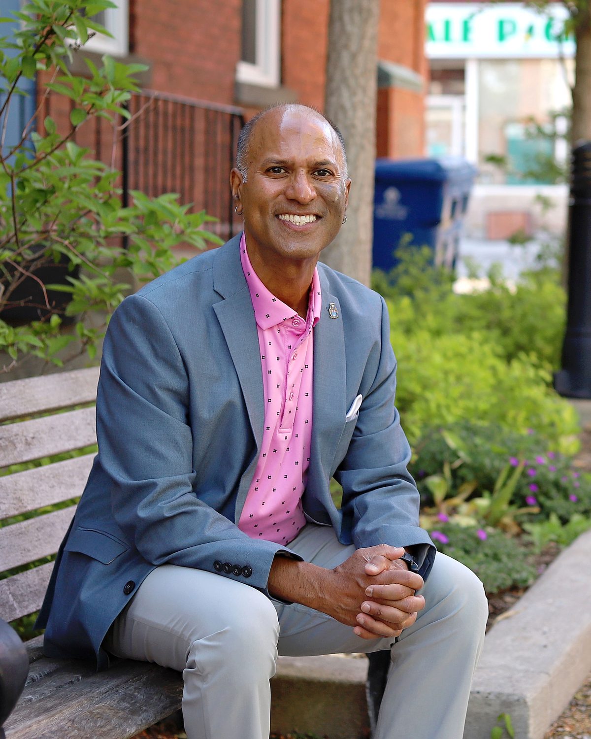 David Parmer seated on a bench on a leafy Stouffville street, hands clasped, smiling