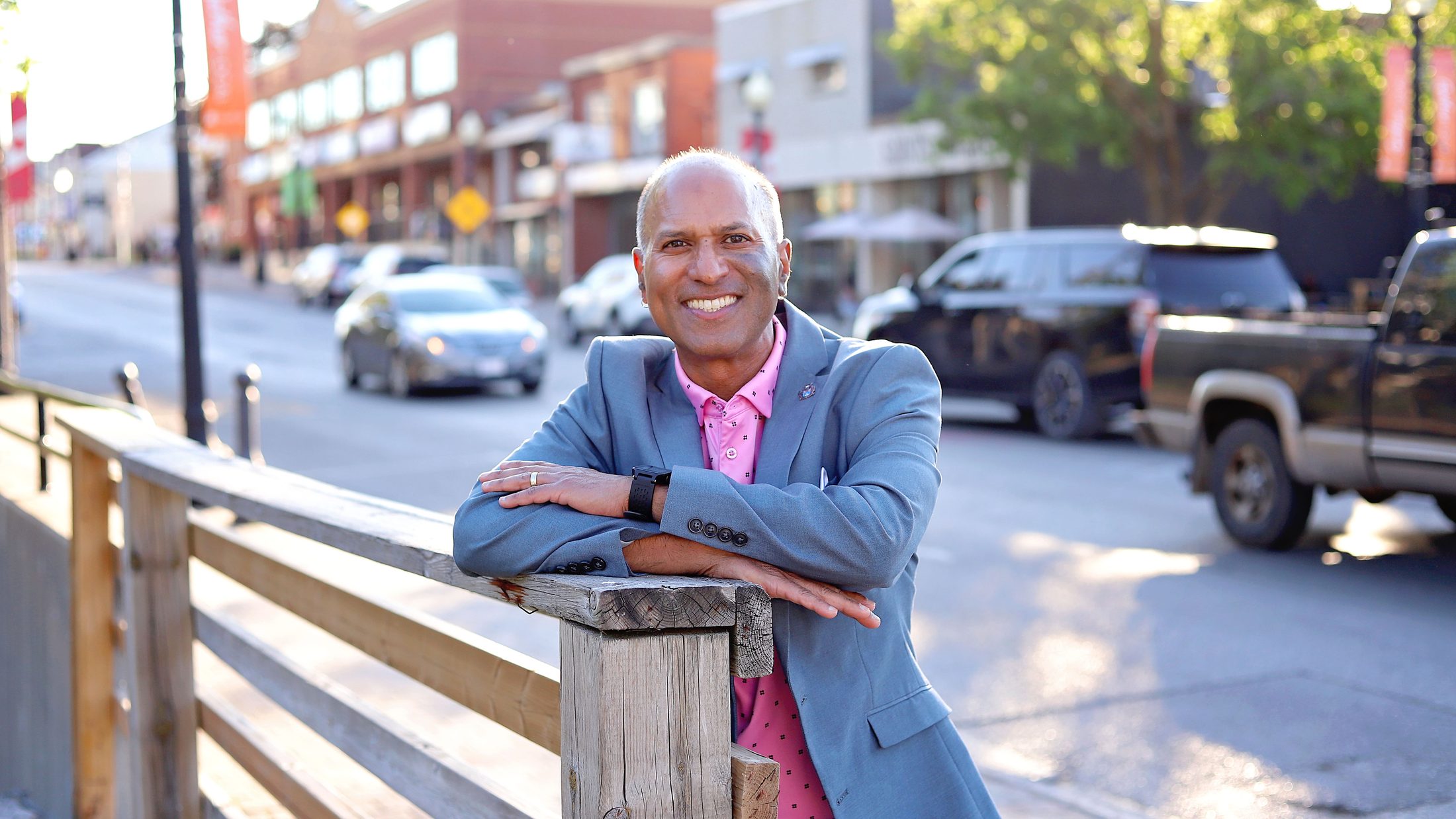 David Parmer leaning on a wooden rail on Main Street in downtown Stouffville, smiling, with the shops of the historic main street behind him