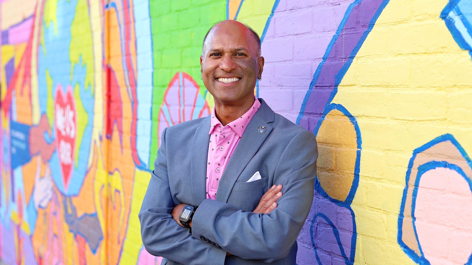 David Parmer standing with arms crossed in front of a colourful community mural
